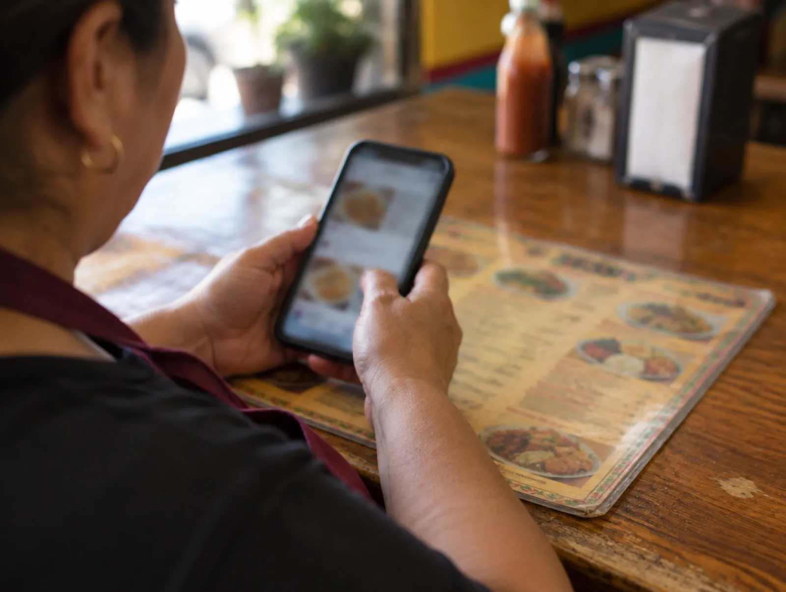 Hands holding a phone over a printed restaurant menu on a wooden counter